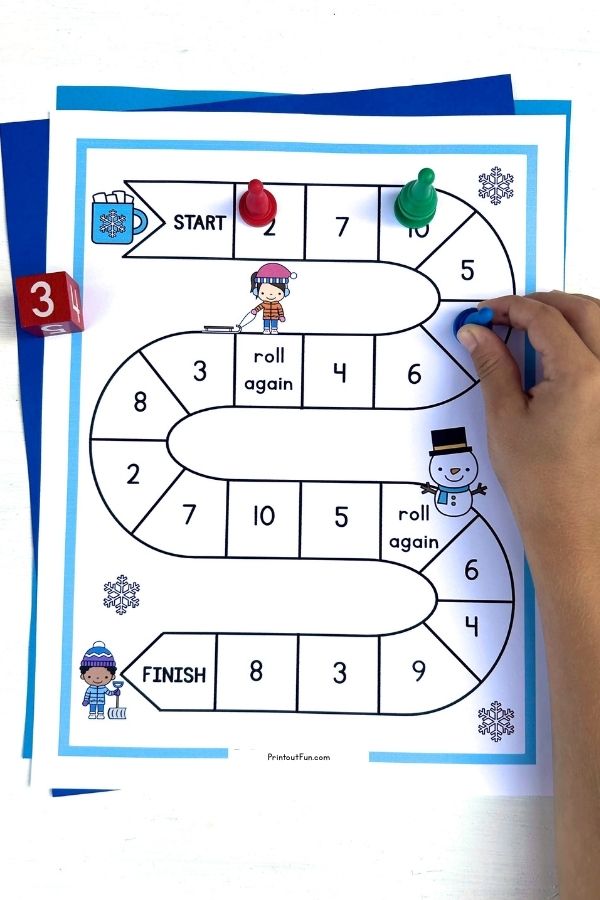 A child's hand moving a game pawn on the 1-10 winter number recognition game board.
