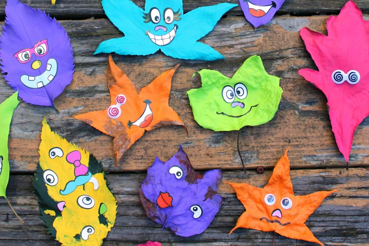 A collection of painted leaves with silly faces laying on a wooden table.