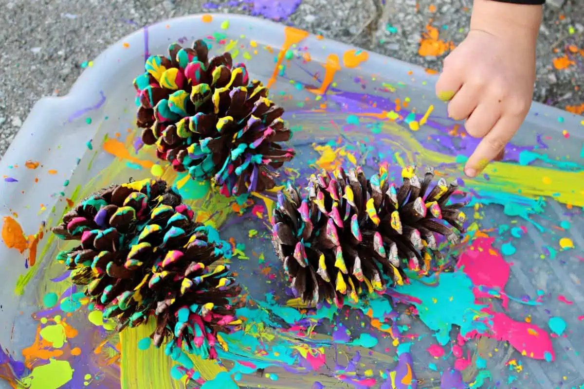A child pointing to 3 examples of splatter painted pine cone art.